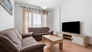 Ein Wohnzimmer mit einer Couch, einem Couchtisch, einem Fernseher auf einem Holzschrank und einem Fenster mit Vorhängen.