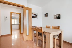 Un comedor con una mesa y sillas de madera, una cocina al fondo y dos cuadros en la pared.