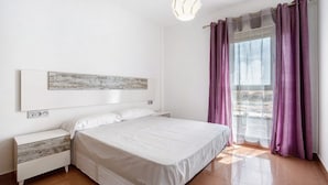 Ein Schlafzimmer mit Bett, Nachttisch, Wandleuchte, Fenster mit Vorhängen und Blick.