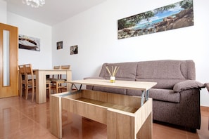 Una habitación con una mesa de comedor de madera, un sofá y un cuadro colgado en la pared que muestra una playa.