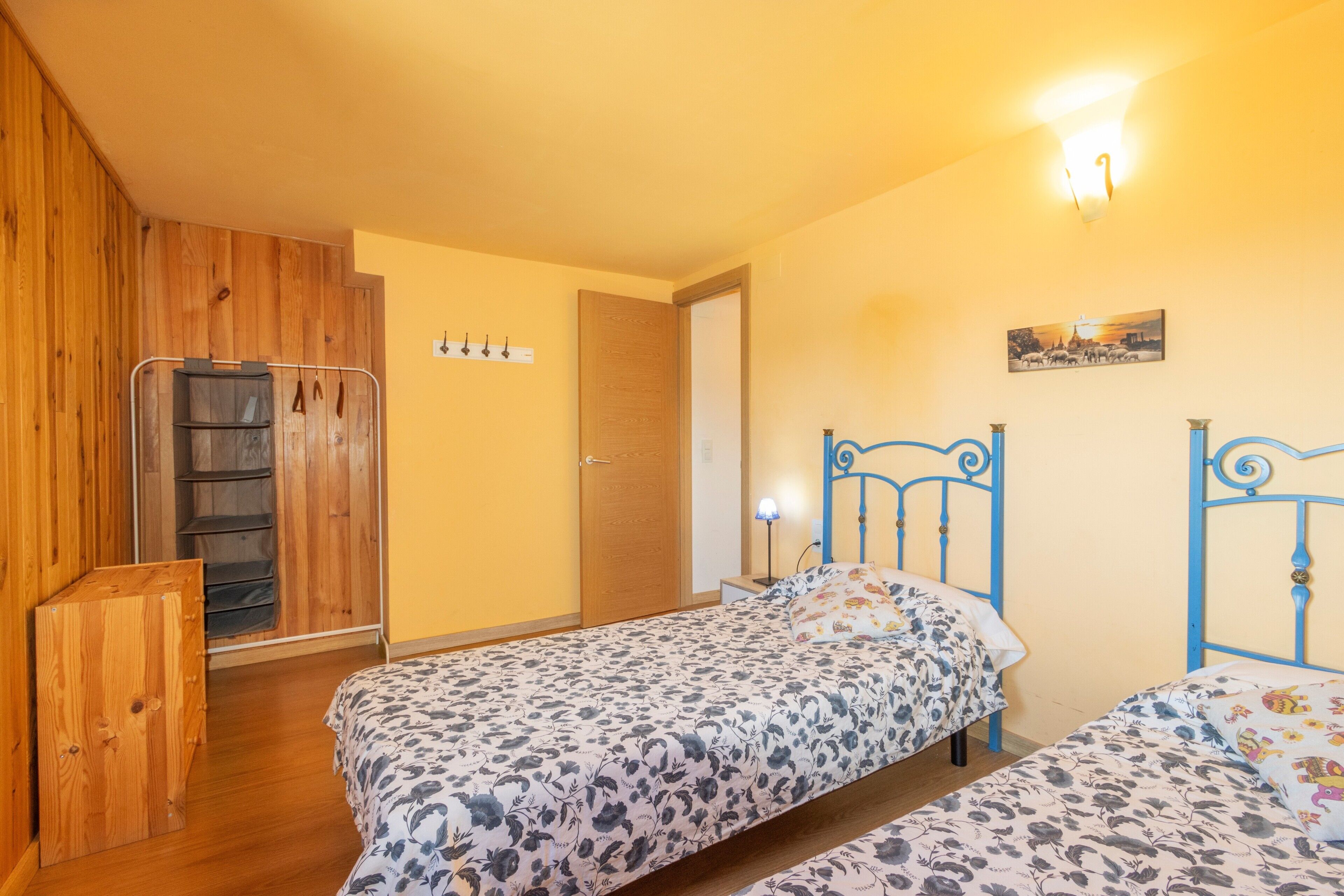 A bedroom with two beds, wooden wardrobe, and a door leading to another room.