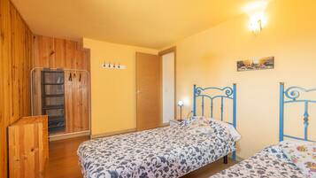A bedroom with two beds, wooden wardrobe, and a door leading to another room.