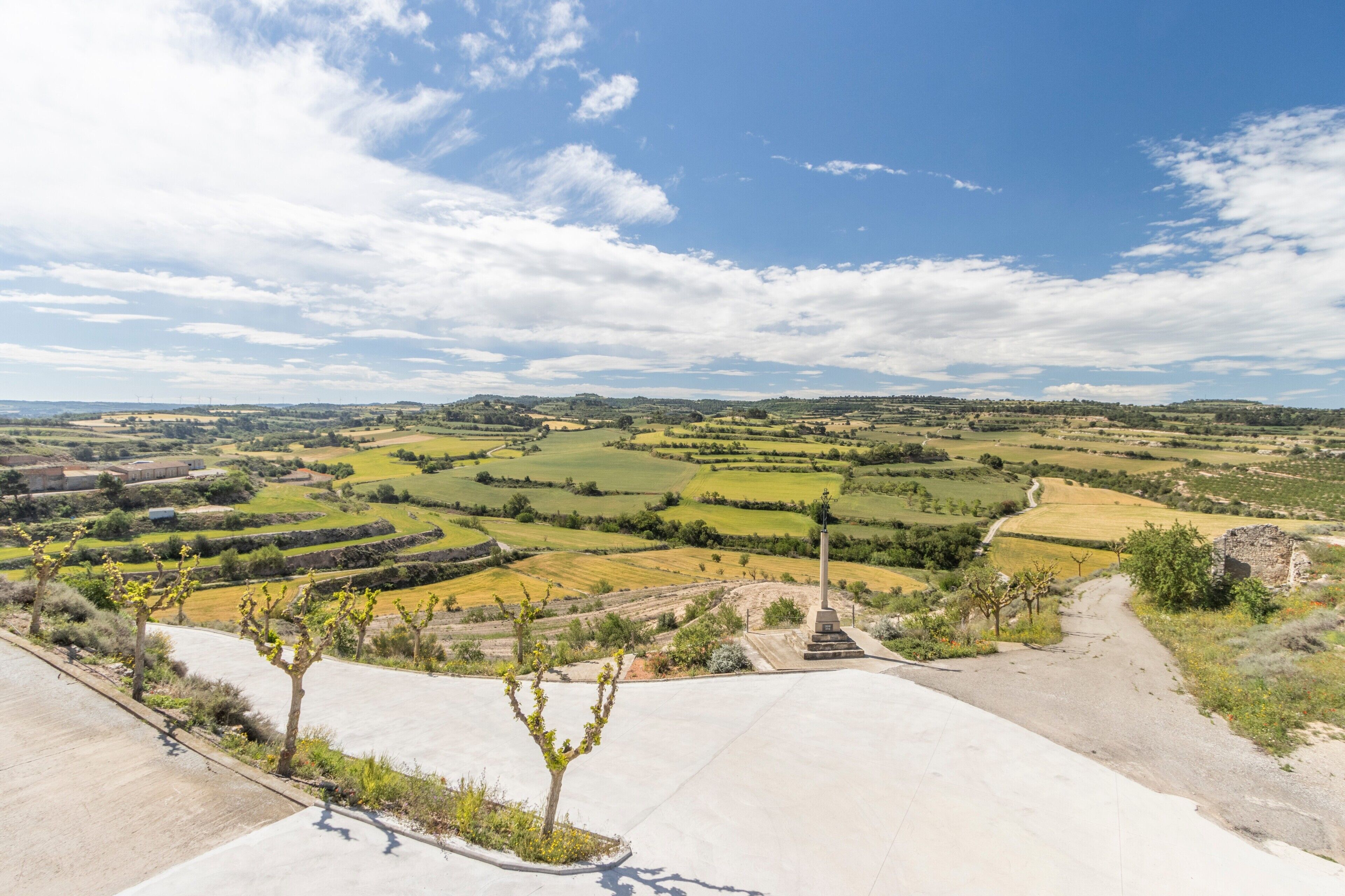 A rural landscape with fields, a monument, and a paved area.