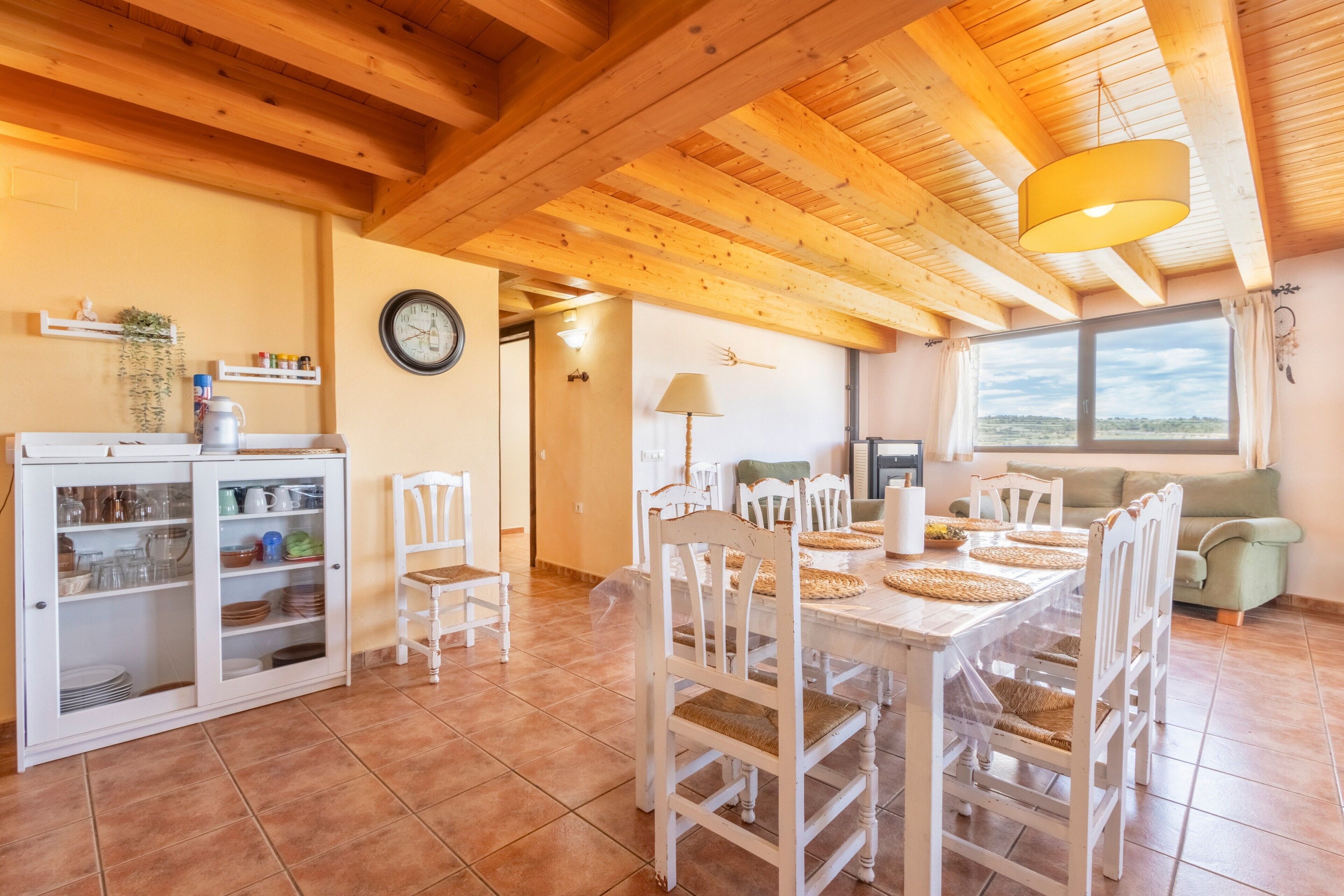 A dining area with a wooden table and chairs, a cabinet with dishes, and a clock on the wall.