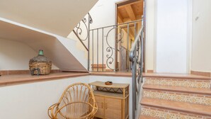 A staircase with patterned tiles, a wicker chair, a wicker basket, and a small table with a decorative item. - Farmhouse 'El Refugi De Rubinat' with Mountain View, Wi-Fi and Air Conditioning (Rubinat)