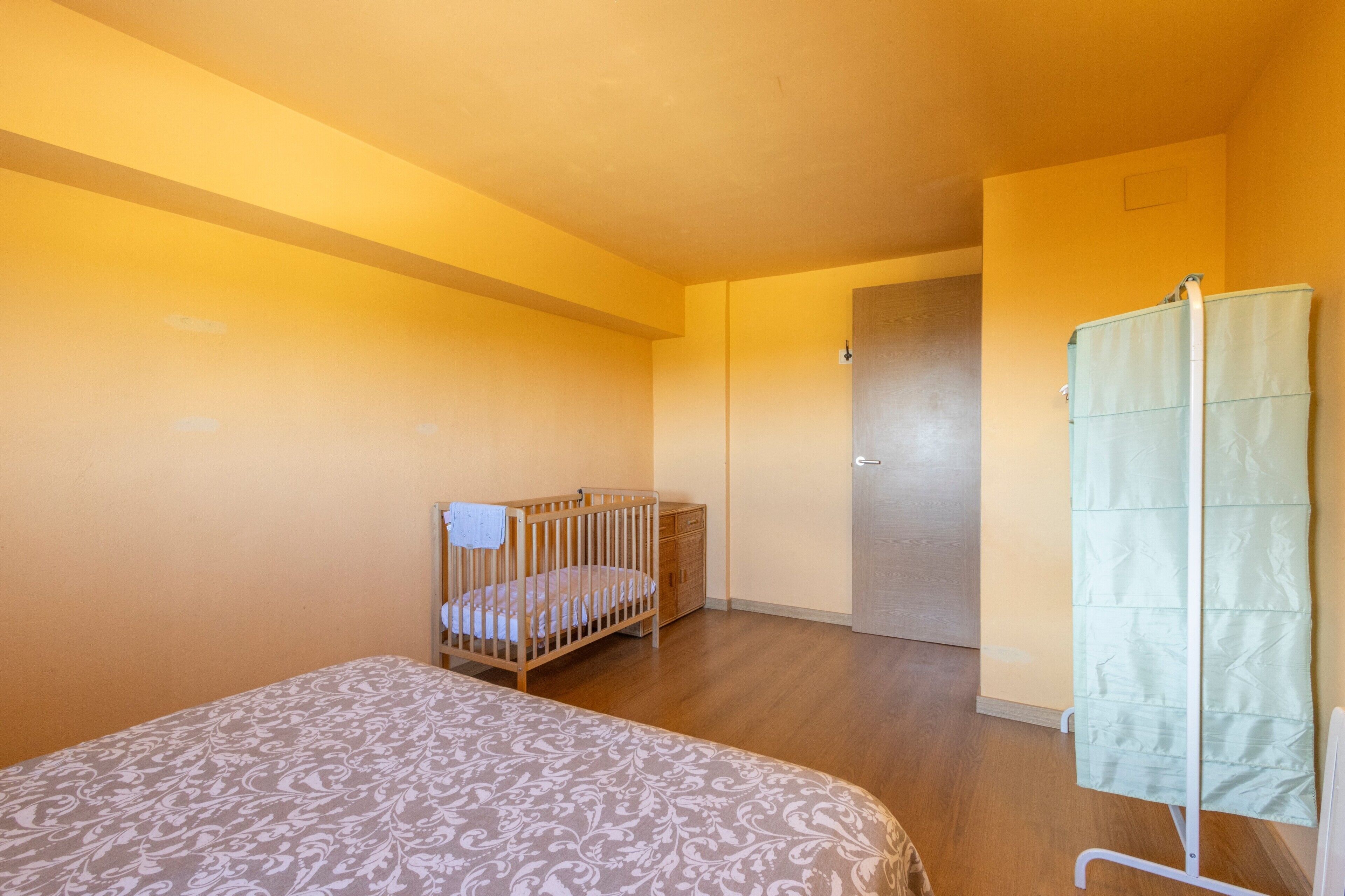 Ein Zimmer mit einem Kinderbett, einem Bett mit gemustertem Überwurf, einem Kleiderschrank und einer Tür.