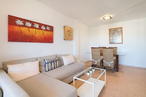 Ein Wohnzimmer mit einer Couch, einem Couchtisch und Sesseln. An der Wand hängt ein Gemälde und auf einem kleinen Tisch steht eine Pflanze.
