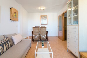 Una sala de estar con un sofá, una mesa de centro con una planta, una mesa de comedor con sillas y un mueble con cajones.