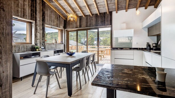 Een moderne keuken met een groot eiland, houten balken en uitzicht op de omgeving.