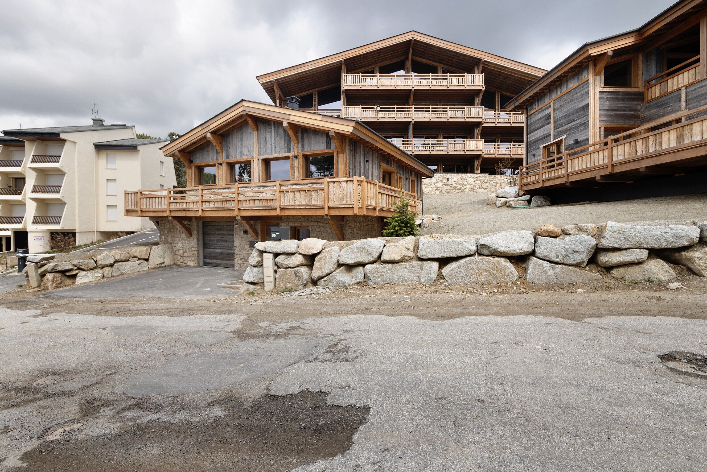 A wooden chalet with balconies, stone walls, and a paved ground.