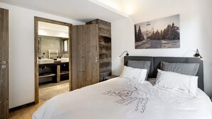 Een slaapkamer met een bed, nachtkastje, een wandlamp, een schilderij en een houten garderobe.
