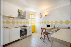 Une cuisine avec des armoires blanches, une cuisinière, un four à micro-ondes et une chaise en bois.