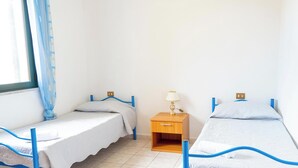 Una stanza con due letti singoli, un comodino con una lampada e una finestra con tende.