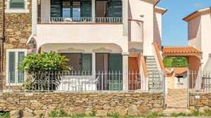 Un edificio a due piani con facciata in pietra, un balcone con ringhiera in metallo e una scala che conduce al piano superiore.