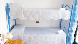 Uma cama de solteiro com roupa de cama branca, uma luminária de cabeceira e uma tomada na parede.
