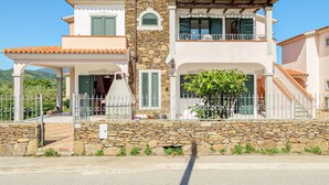 Uma casa de dois andares com fachada de pedra, varanda e alpendre coberto.