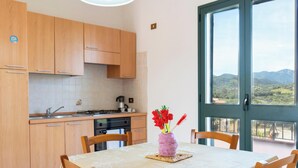 Cozinha com armários de madeira, uma mesa de jantar com um vaso de flores e vista através de uma janela grande.