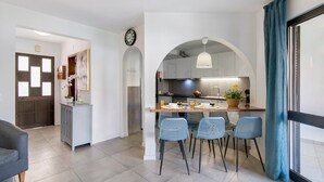 Une cuisine moderne avec un îlot central, des chaises bleues et une horloge au mur.