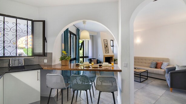 Une cuisine moderne avec un coin bar, une table à manger avec des chaises et un espace salon comprenant un canapé et une table basse.