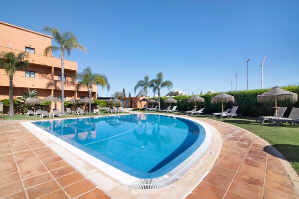A swimming pool with lounge chairs and palm trees, surrounded by a building with balconies. - Villa 'Casa Sol' with Shared Pool, Private Terrace and Wi-Fi (Quarteira)