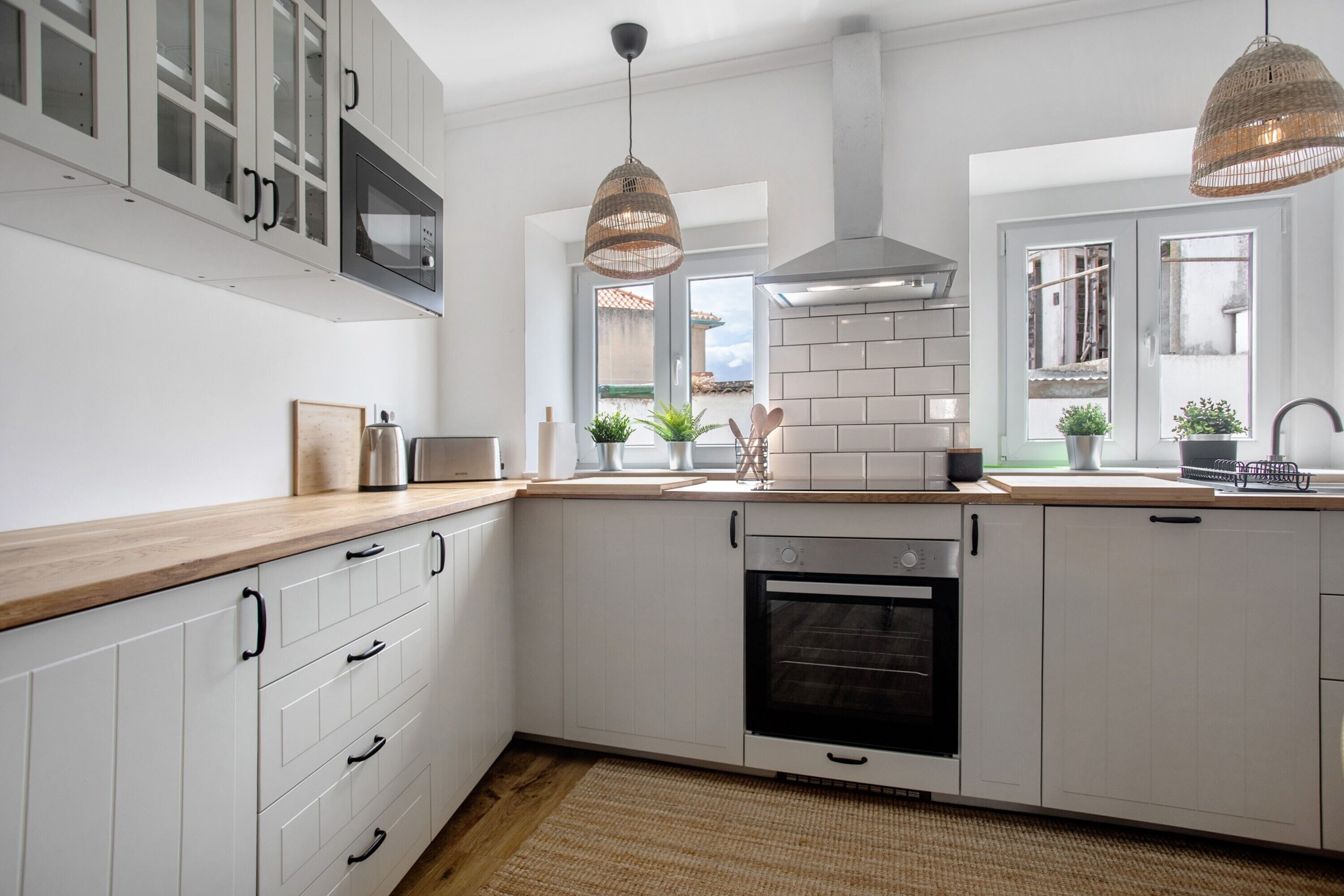 Una cocina moderna con armarios blancos, horno empotrado, microondas e iluminación colgante.