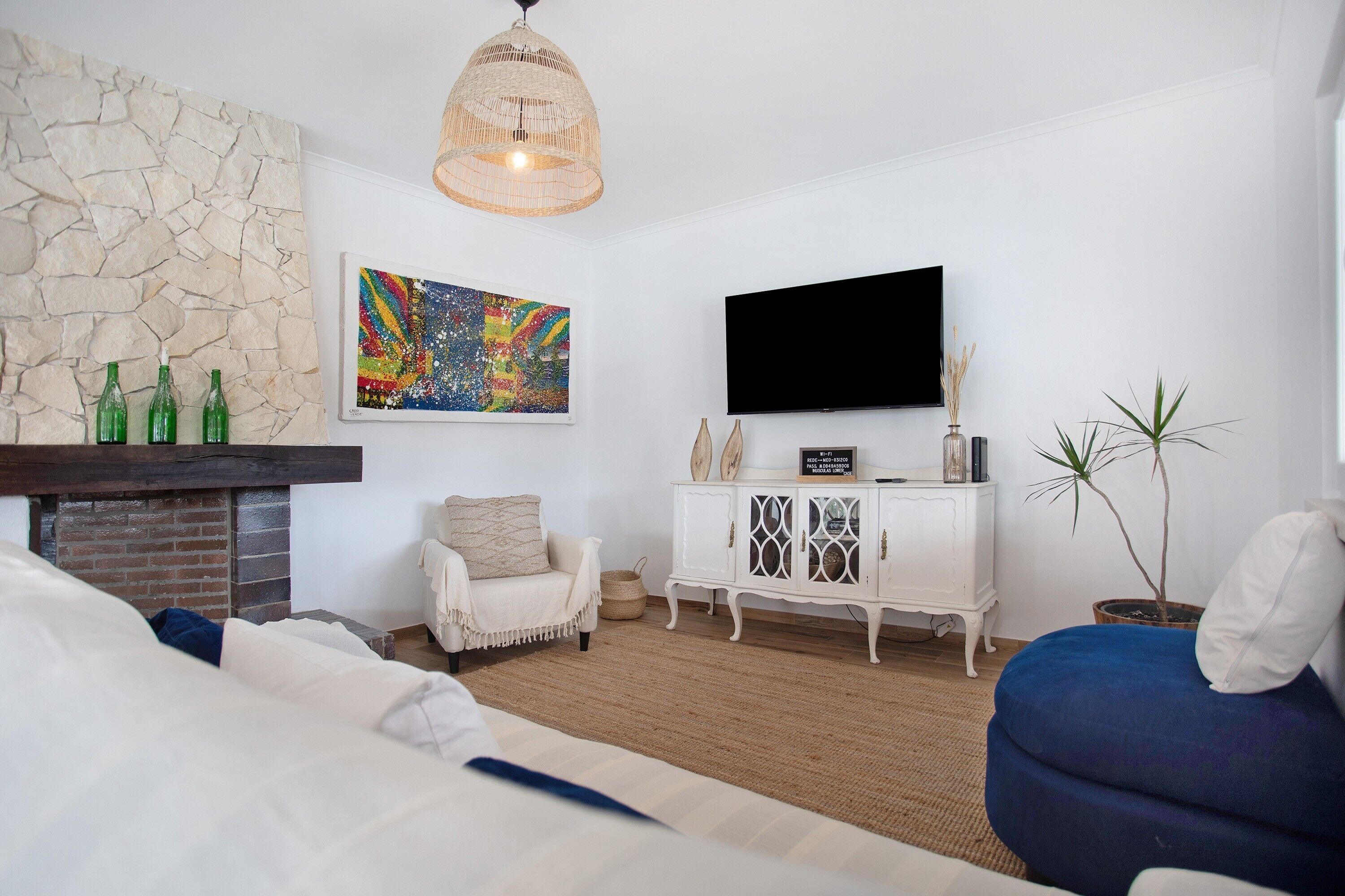 A room with a fireplace, a television, a sofa, a cabinet, and a painting.
