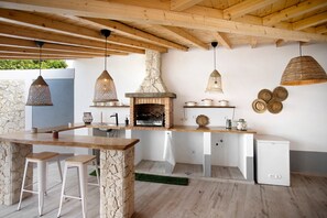 Een rustieke keuken met een stenen muur, houten balken, hangende lampen, een inbouwoven en een kleine koelkast.