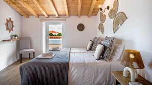 A bedroom with a wooden ceiling, two beds, a chair, a bedside table with a lamp, and a view of a building outside. - Holiday Home 'Vila River Sublime' with Private Pool, Wi-Fi and Air Conditioning (Valada)