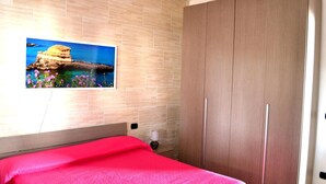 A bedroom with a bed, a wooden wardrobe, and a wall-mounted picture of a coastal landscape. - Villa 'Ll04 Hikari with Outdoor Spaces', Private Garden, Wi-Fi & Air Conditioning (San foca)