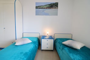 Une chambre avec deux lits, une table de chevet, une lampe et un tableau représentant une plage.