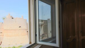 Une pièce dotée d’une fenêtre donnant sur une tour de pierre historique, une porte en bois et une vue sur un balcon avec une balustrade.
