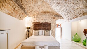 Une chambre avec un plafond en pierre, un lit recouvert de draps blancs, une table de chevet et un vase vert posé sur la table de nuit.