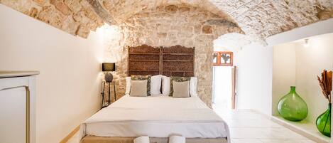 A bedroom with a stone ceiling, a bed with white linens, a bedside table, and a green vase on the nightstand.