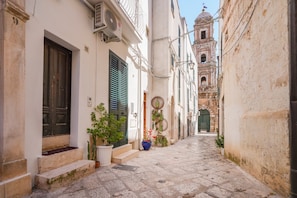 A narrow cobblestone street flanked by historic buildings with a bell tower in the distance.