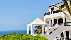 A modern two-story building with balconies, a white facade, and a view of the sea. - Apartment with Stunning Ocean View, Pool, Garden, Terrace & Wi-Fi (Costa del Silencio)