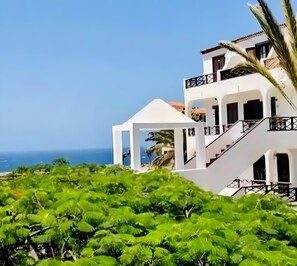 A modern two-story building with balconies, a white facade, and a view of the sea. - Apartment with Stunning Ocean View, Pool, Garden, Terrace & Wi-Fi (Costa del Silencio)