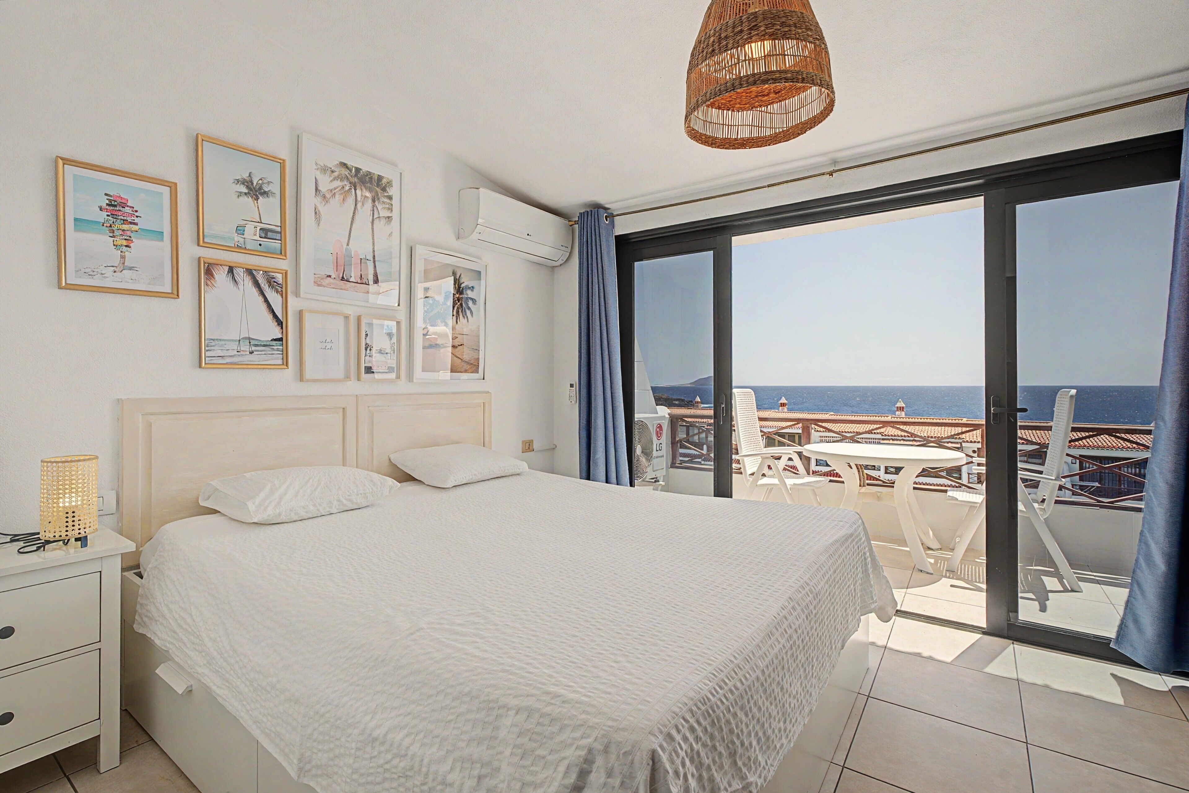 Une chambre avec un lit, une table de chevet, un climatiseur fixé au mur et une grande fenêtre donnant sur la mer.