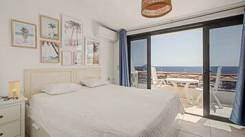 Une chambre avec un lit, une table de chevet, un climatiseur fixé au mur et une grande fenêtre donnant sur la mer.