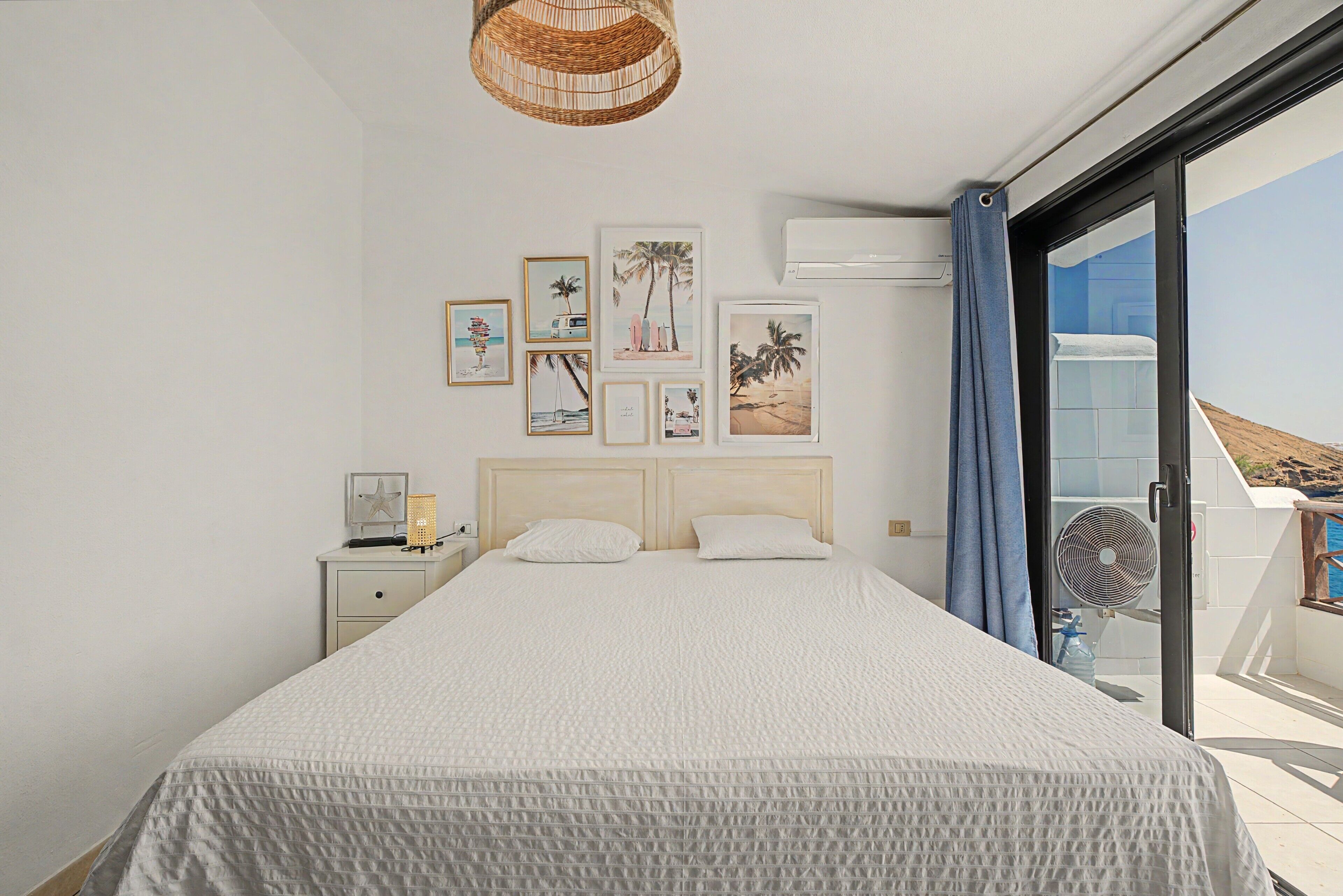 Un dormitorio con cama, mesita de noche, aire acondicionado instalado en la pared y ventana con vista al mar.