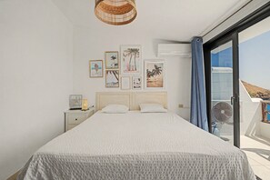 Un dormitorio con cama, mesita de noche, aire acondicionado instalado en la pared y ventana con vista al mar.
