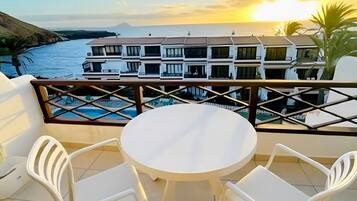 A balcony with a round table and two chairs, overlooking a body of water and a building complex.