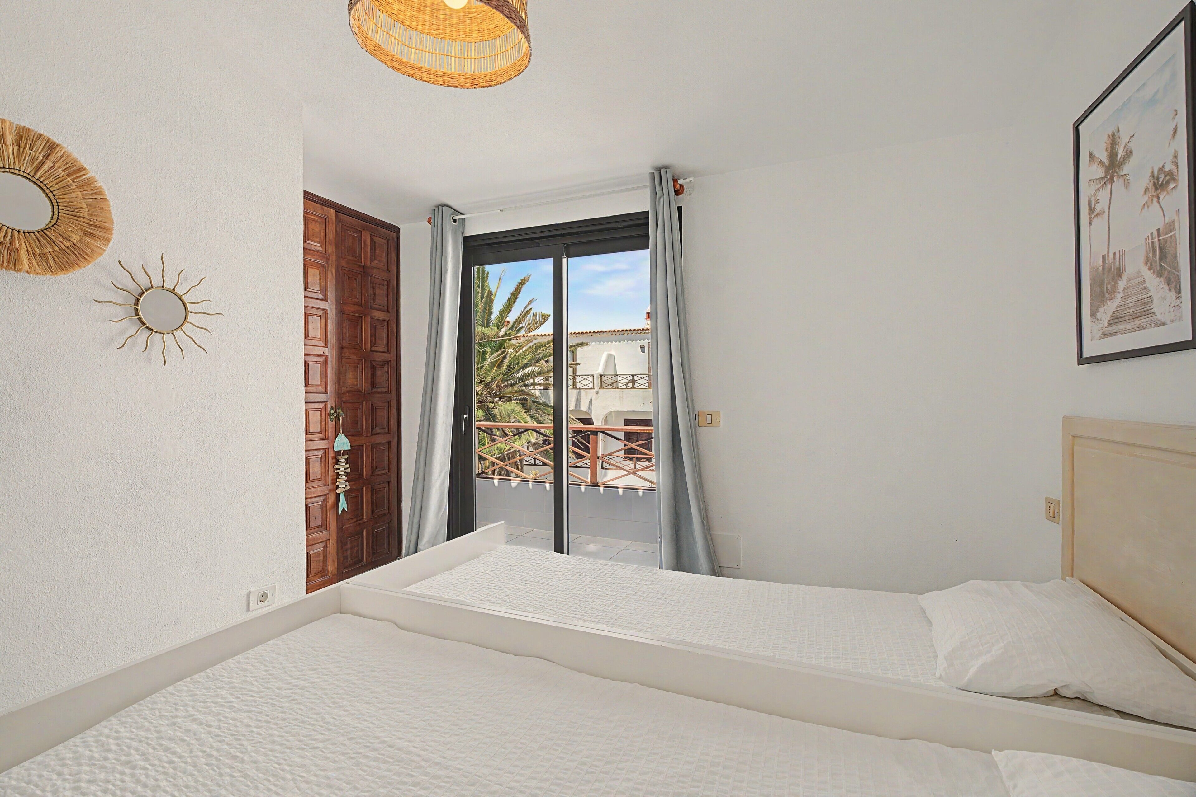 A bedroom with a bed, a window with a view of a balcony, and a door leading outside.