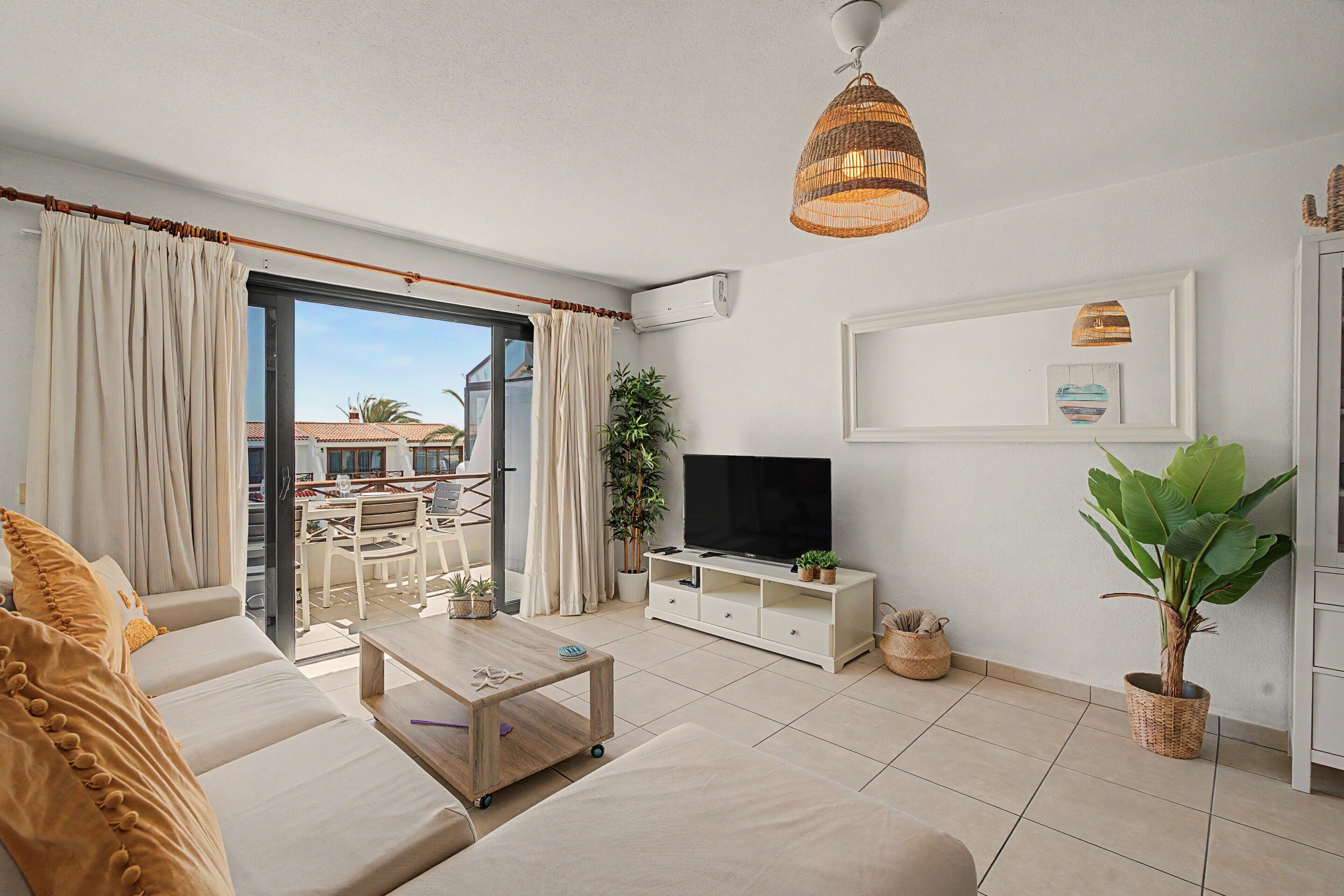 Una sala de estar con sofá, mesa de centro, mueble para la televisión y un balcón con cortinas.