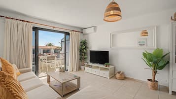Una sala de estar con sofá, mesa de centro, mueble para la televisión y un balcón con cortinas.