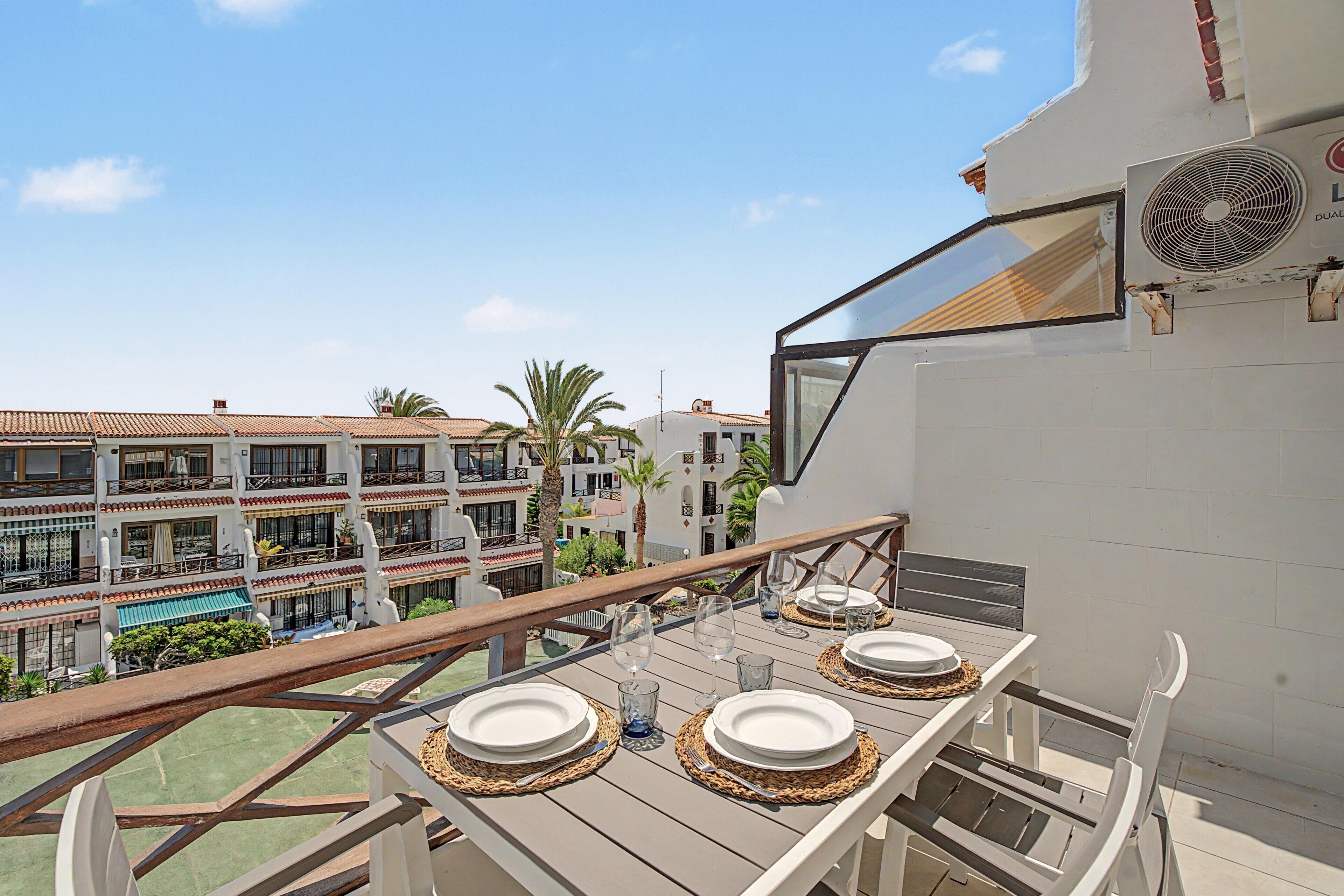 Een balkon met een eettafel, met uitzicht op een woongebied met meerdere gebouwen en palmbomen.