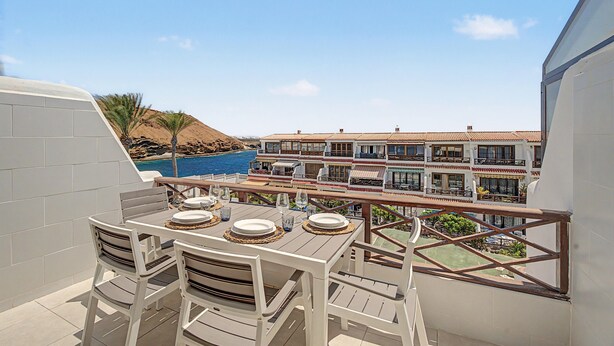 A balcony with a table set for dining, overlooking a pool and a building with multiple balconies. - Apartment with Stunning Ocean View, Pool, Garden, Terrace & Wi-Fi (Costa del Silencio)