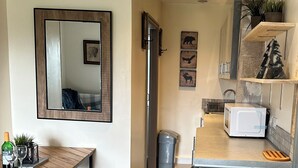 A compact kitchen with a microwave, a sink, and a small countertop. There is a mirror on the wall and a framed picture above it.