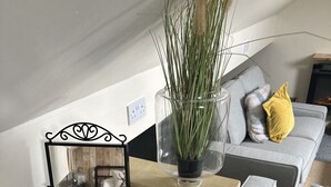 A wooden chest with plants, a mirror, and a grey sofa with a yellow pillow in a living room. - Charming 1-Bed Apartment in Hereford (Hereford)
