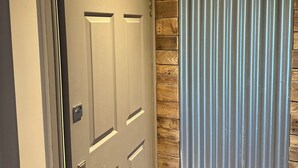 A door with a sign indicating a toilet, a wooden panel wall, and a metal curtain. - Charming 1-Bed Apartment in Hereford (Hereford)