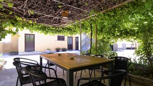 An outdoor patio with a wooden table and black wicker chairs, surrounded by greenery and a stone floor. - Holiday apartment with air conditioning (Fažana)